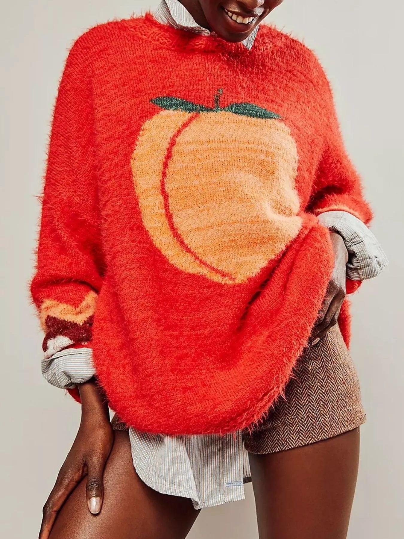 Person wearing a red sweater with a pumpkin design on a plain background