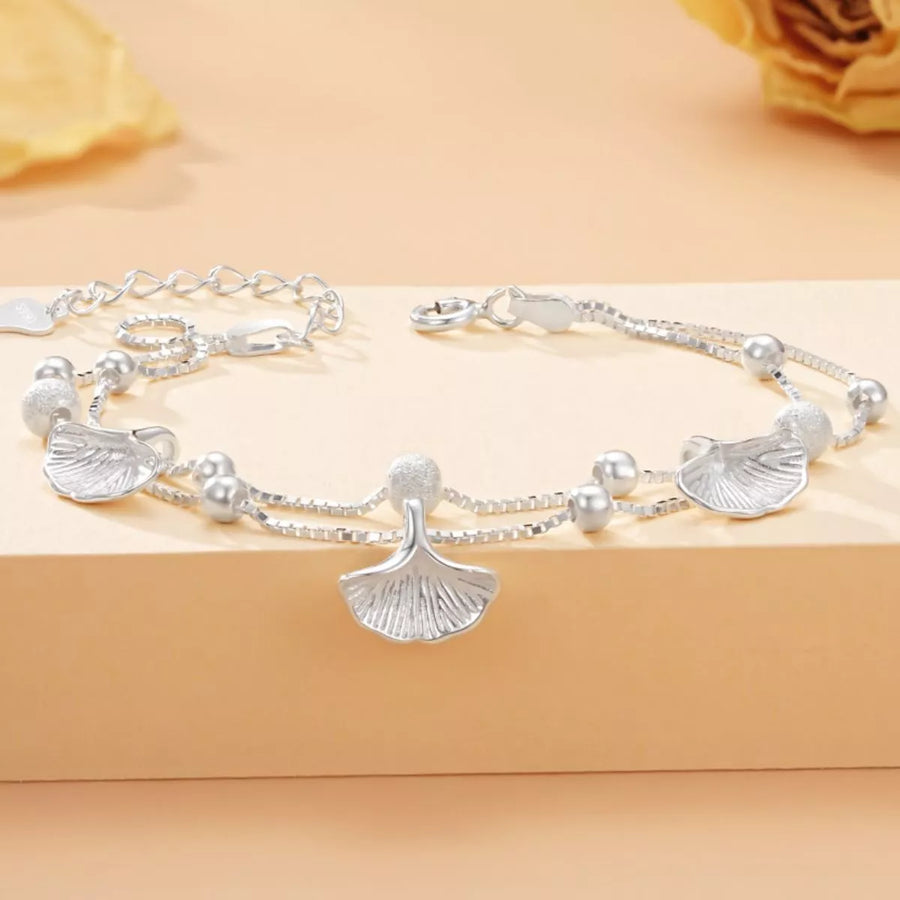 Silver bracelet with leaf-shaped charms on a beige background