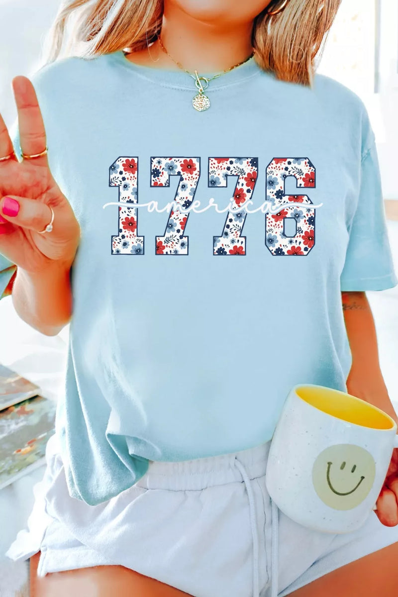 Person wearing a light blue t-shirt with '1776' design, holding a mug with a smiley face.