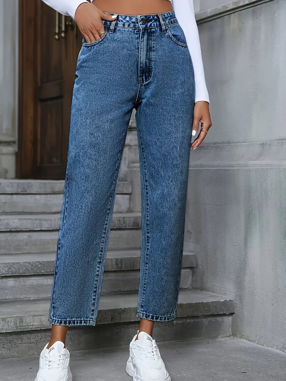 Person wearing blue jeans and white sneakers standing on steps.