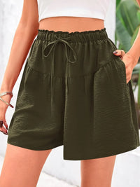 Person wearing olive green shorts with a white top and blurred background
