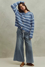 Woman wearing a blue and white striped sweater and jeans against a neutral background