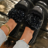 Black slippers with floral decorations worn by a person on a reflective surface.