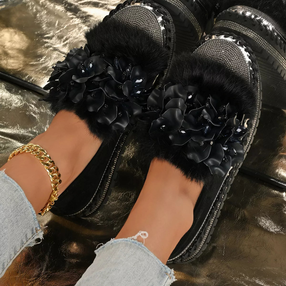 Black slippers with floral decorations worn by a person on a reflective surface.