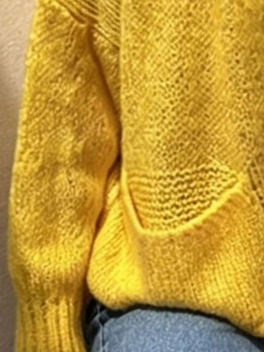 Close-up of a mustard yellow knit sweater with a textured knit pattern and a visible hand pocket, worn over blue jeans.