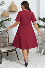 Woman wearing a red dress in an indoor setting with plants and a chair.