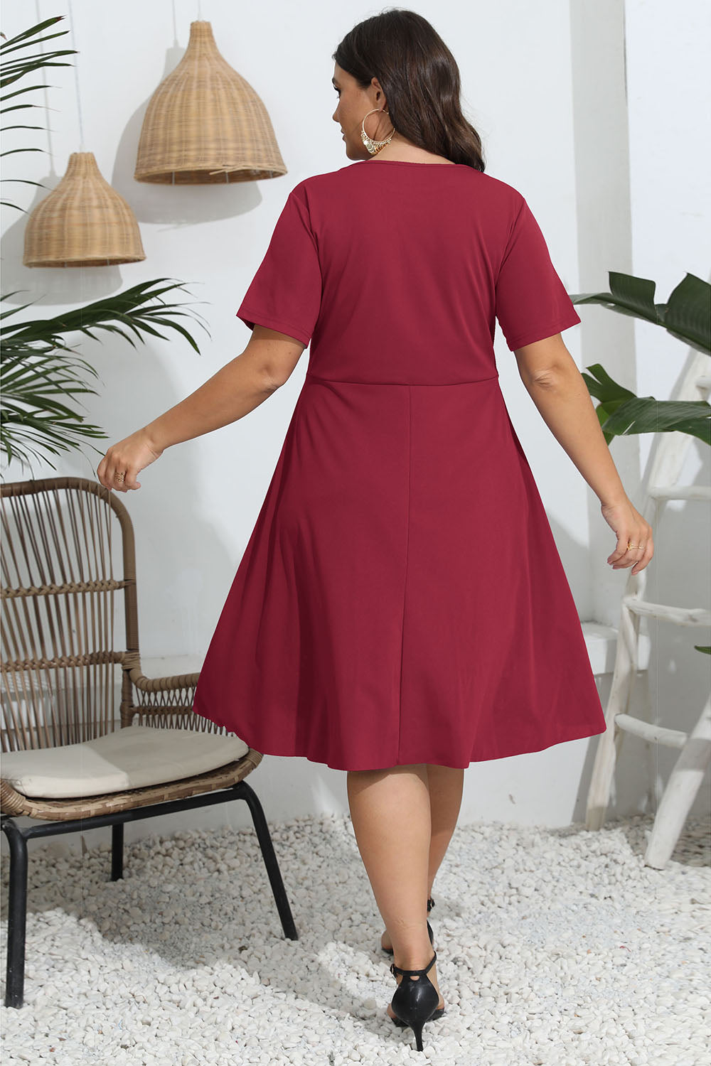 Woman wearing a red dress in an indoor setting with plants and a chair.