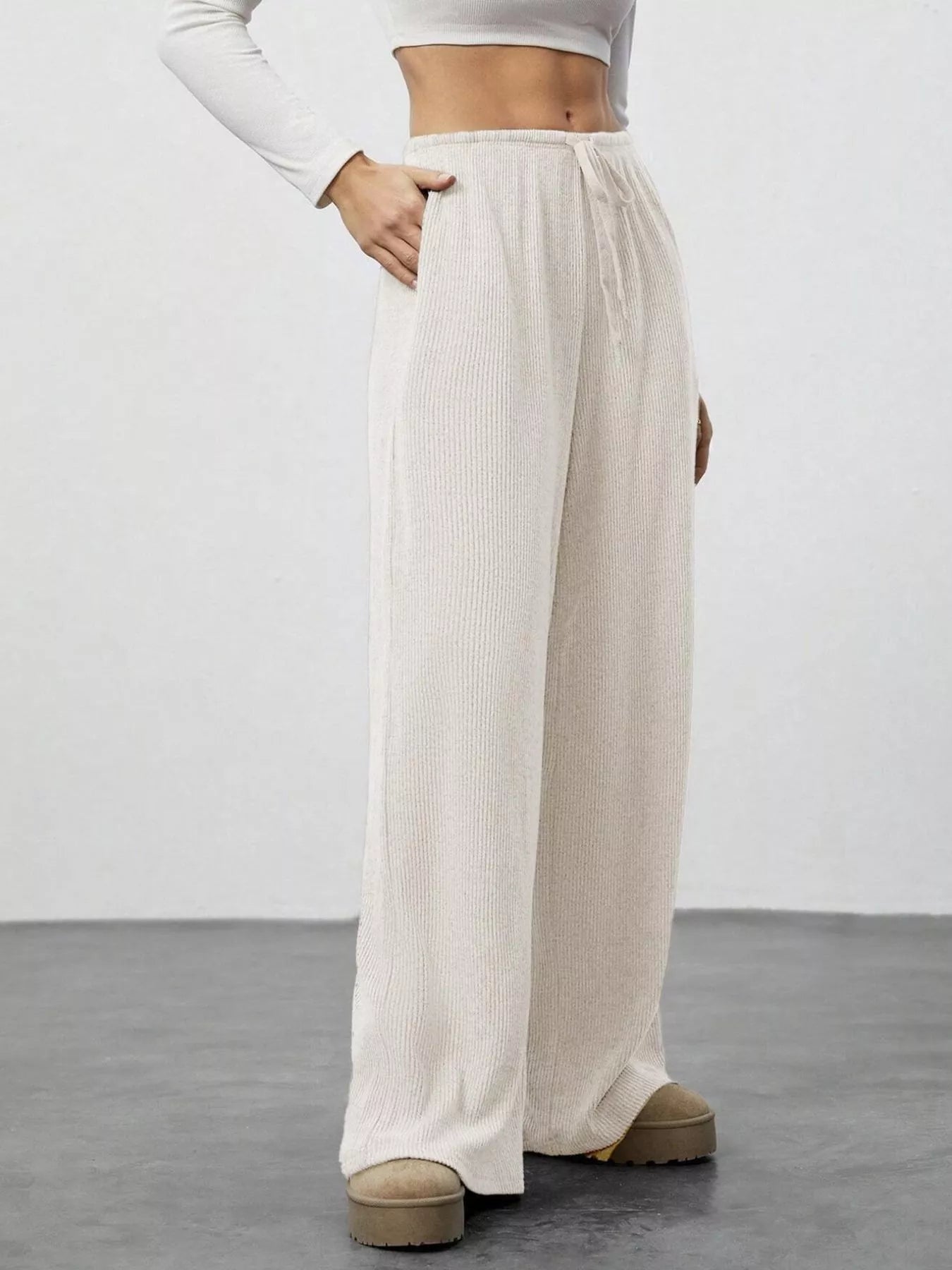 Person wearing beige wide-leg pants and a white long-sleeve top on a plain background