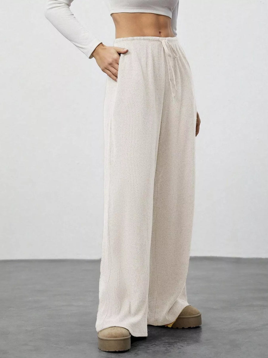 Person wearing beige wide-leg pants and a white long-sleeve top on a plain background