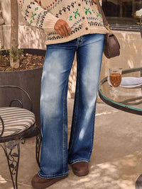 Person wearing a patterned sweater, blue jeans, and brown shoes in an outdoor setting.