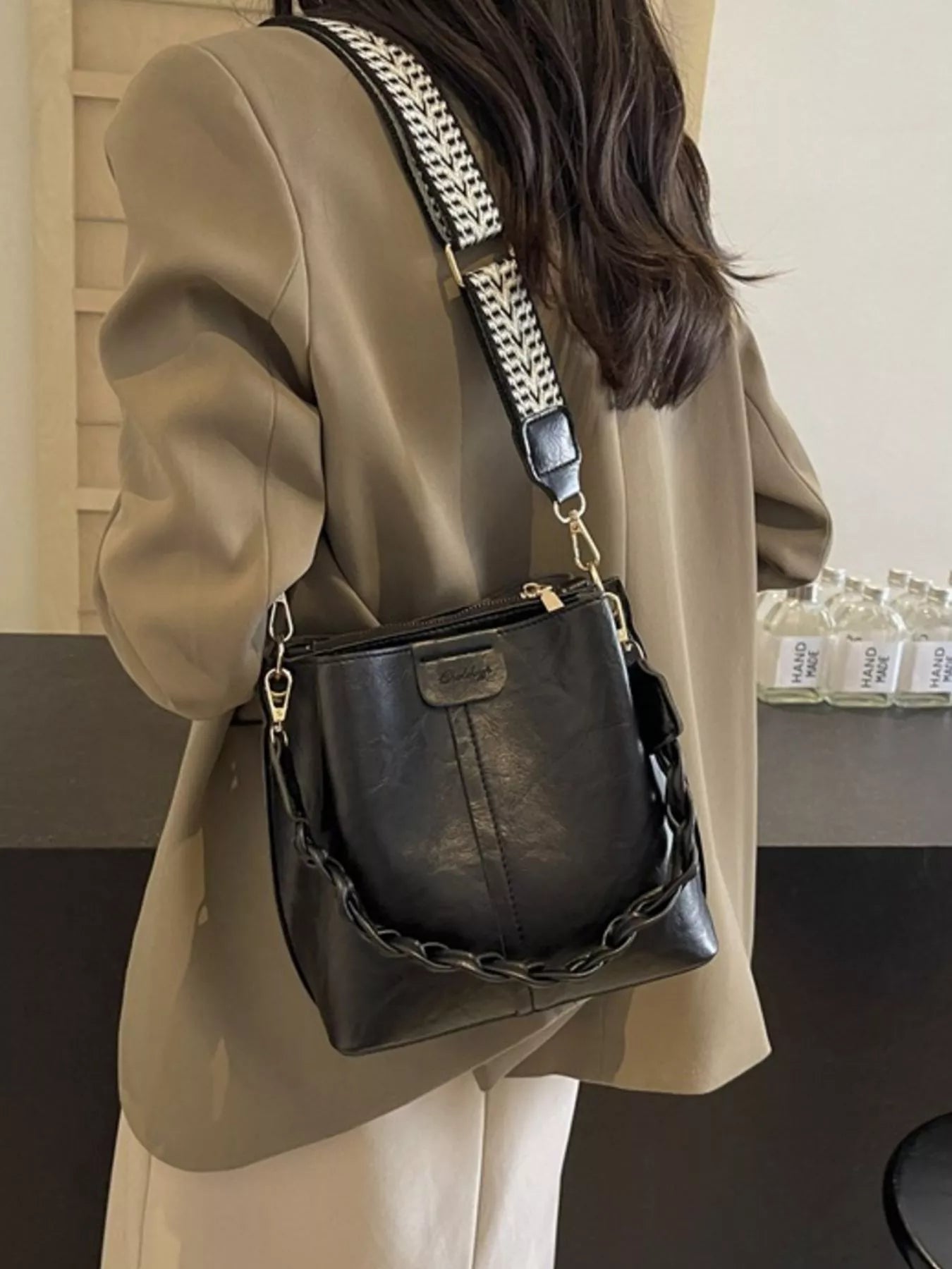 Person wearing a beige coat with a black handbag featuring a chain detail.