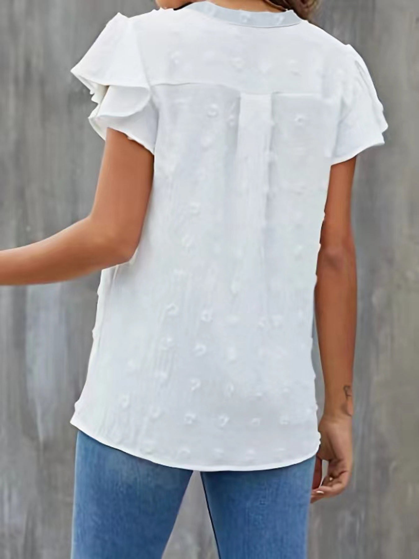 White blouse with ruffled sleeves worn by a person against a gray background