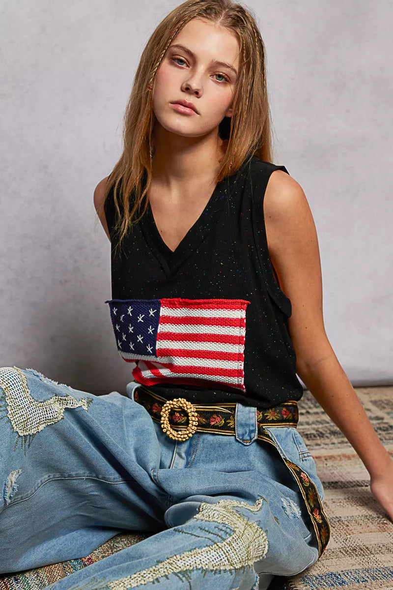 Woman wearing a black sleeveless top with an American flag patch and blue jeans.