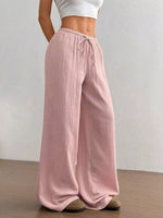 Person wearing pink wide-leg pants with a white top against a plain background
