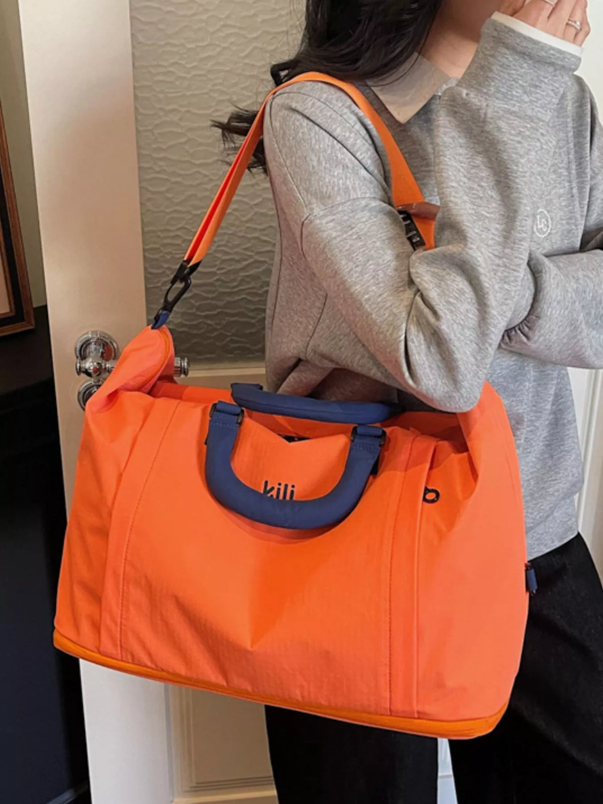 Person holding an orange bag with blue handles indoors