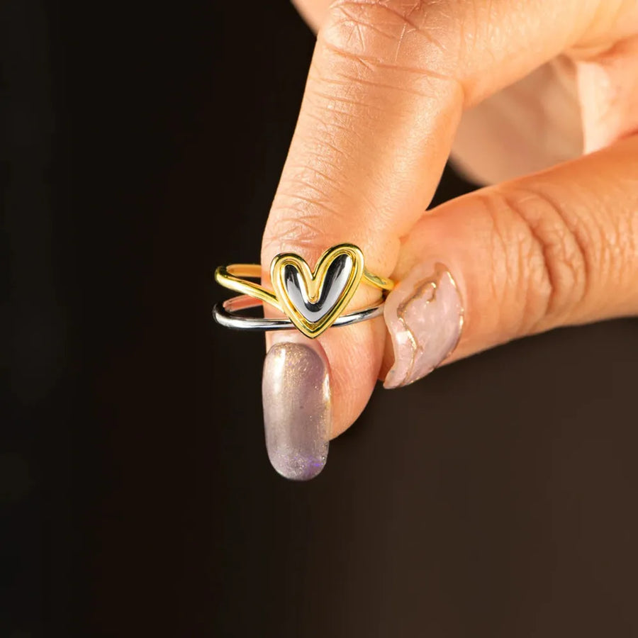 Heart-shaped ring on a finger against a dark background