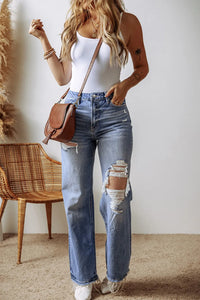 Woman wearing a white bodysuit and blue jeans with a brown bag, standing indoors.