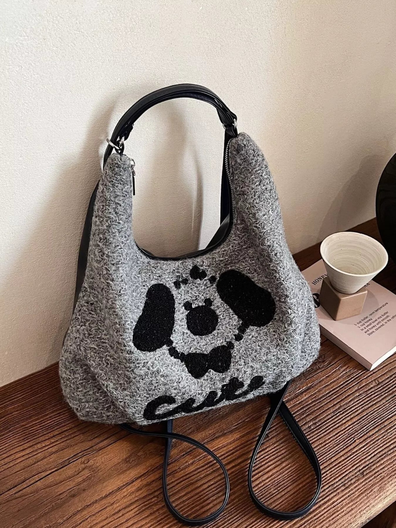 Gray textured handbag with black paw print design on a wooden surface.