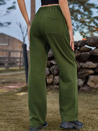 Person wearing green pants standing outdoors with a stone wall and wooden fence in the background