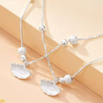 Silver necklace with ginkgo leaf pendants on a beige background