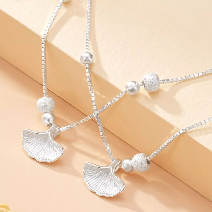 Silver necklace with ginkgo leaf pendants on a beige background
