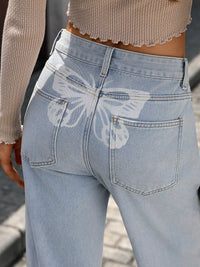 Light blue jeans with a butterfly design on the back pocket worn by a person.