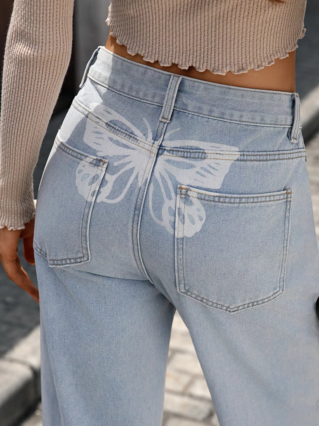 Light blue jeans with a butterfly design on the back pocket worn by a person.