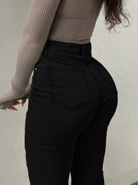 Person wearing black high-waisted jeans and a ribbed long-sleeve top against a neutral background