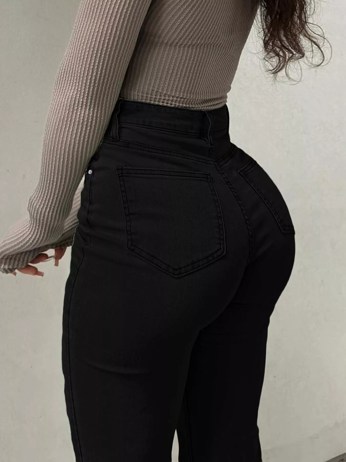 Person wearing black high-waisted jeans and a ribbed long-sleeve top against a neutral background