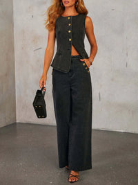 Woman wearing a black sleeveless top and wide-leg pants against a gray concrete wall.