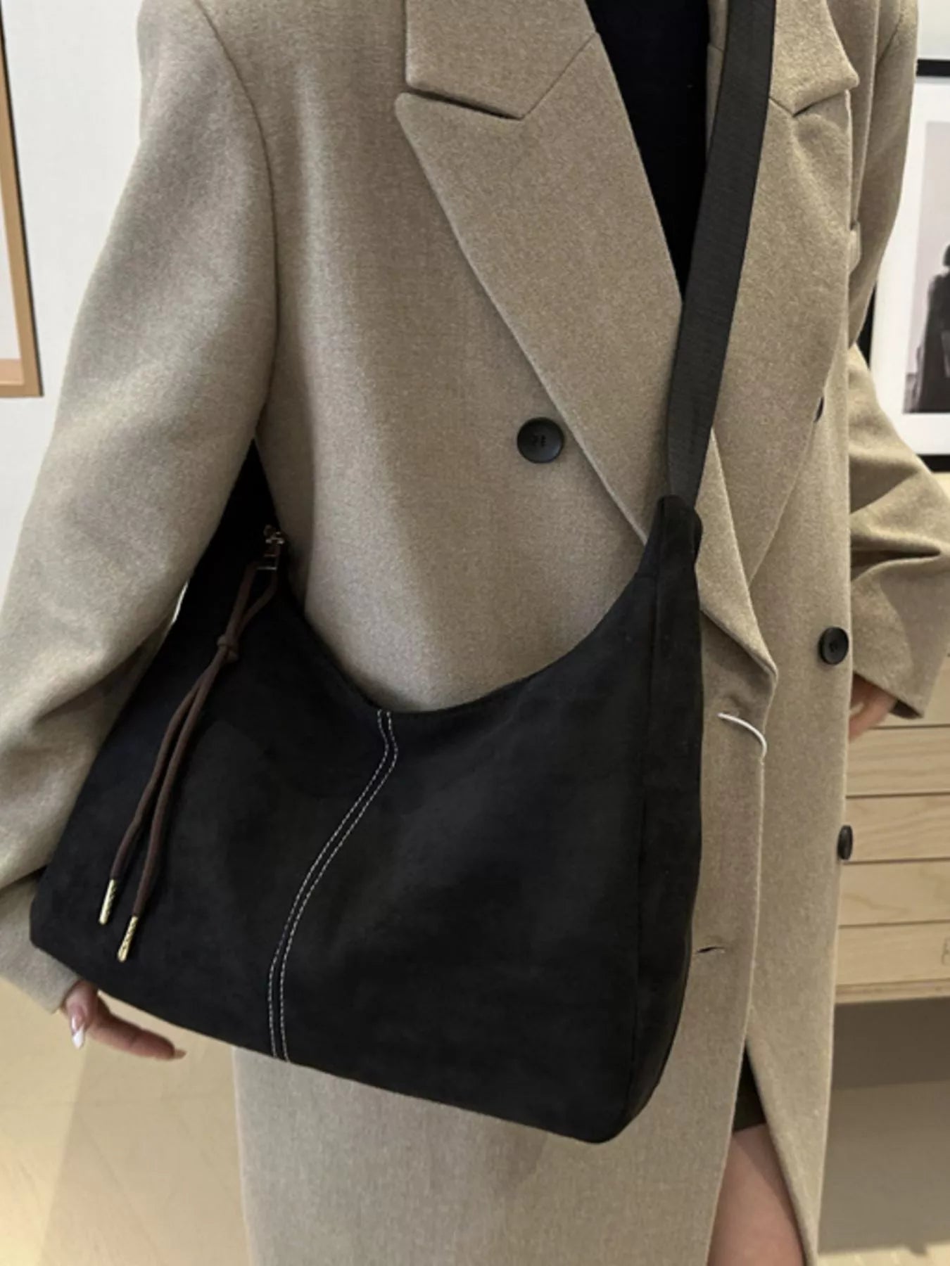 Person wearing a beige coat with a black shoulder bag indoors.