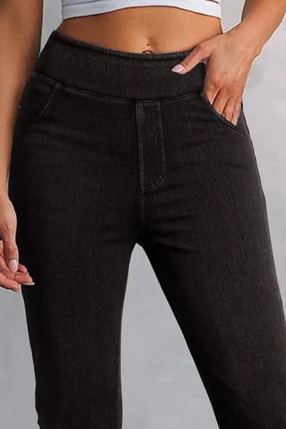 Person wearing black high-waisted jeans on a gray background