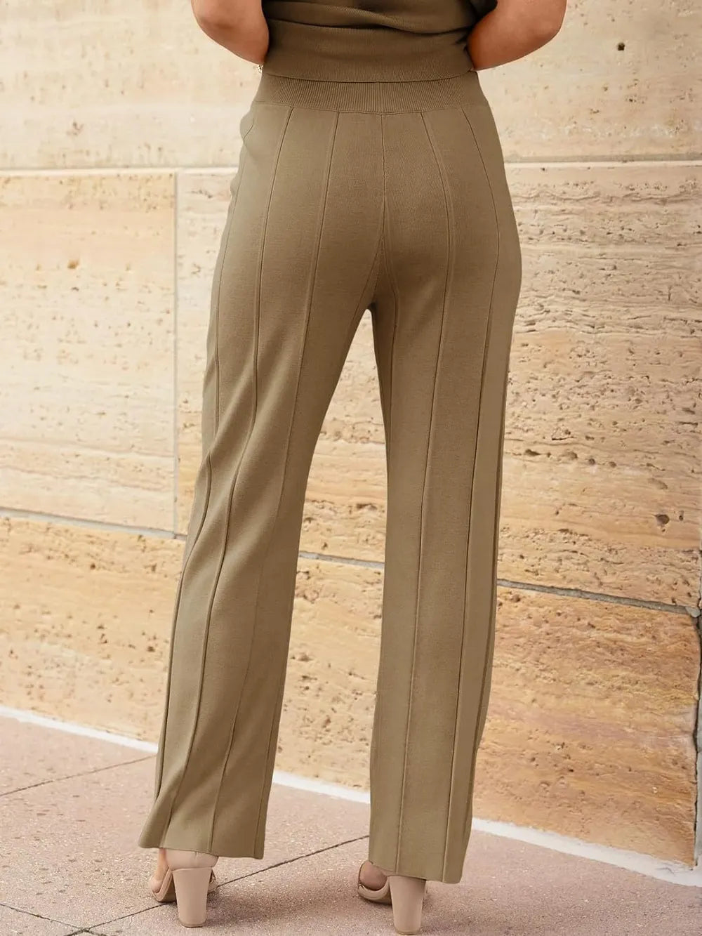 Person wearing beige high-waisted pants against a stone wall.