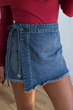 Person wearing a red top and denim skirt on a light wooden floor.