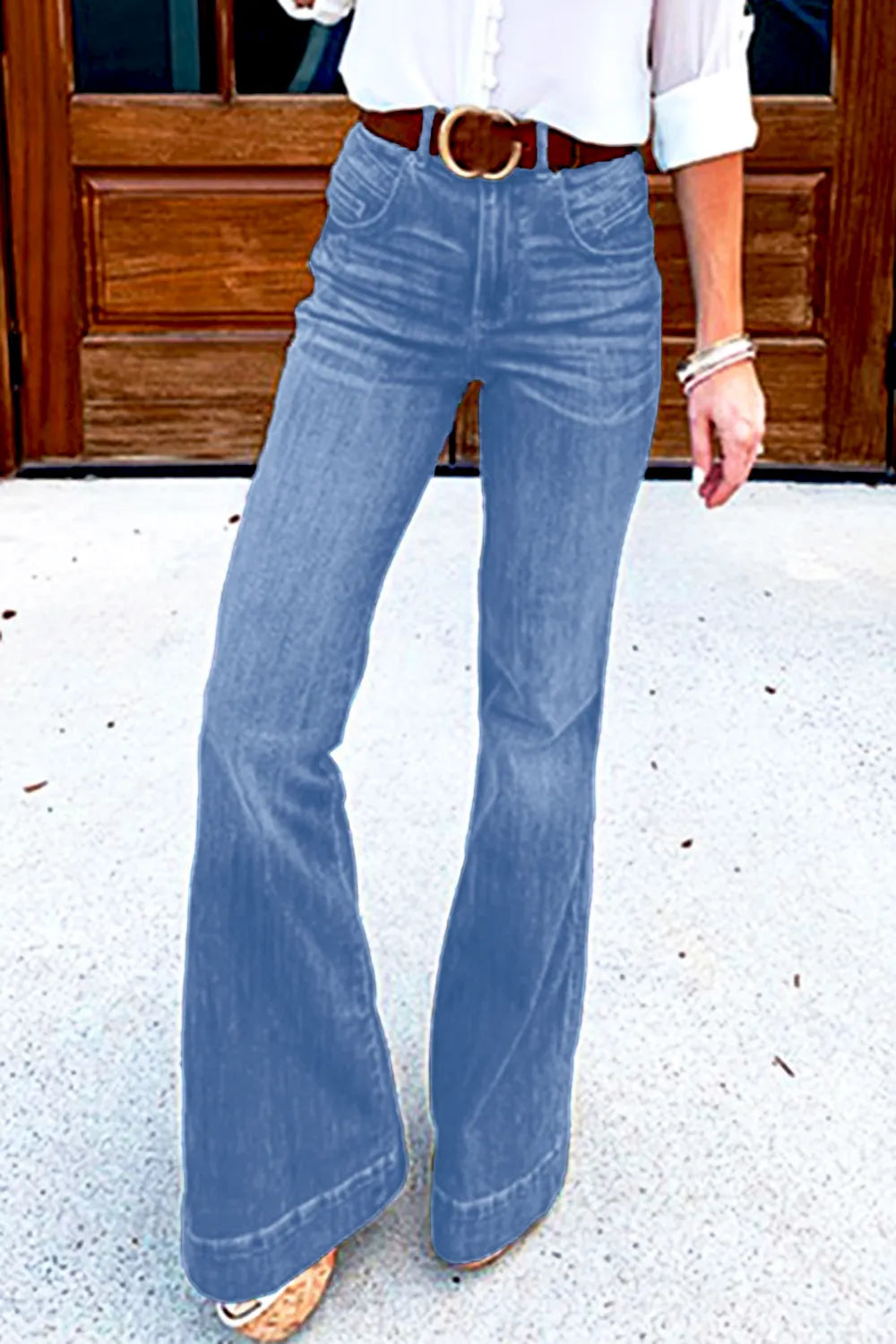 Person wearing blue flared jeans standing on a concrete surface with a wooden door in the background.