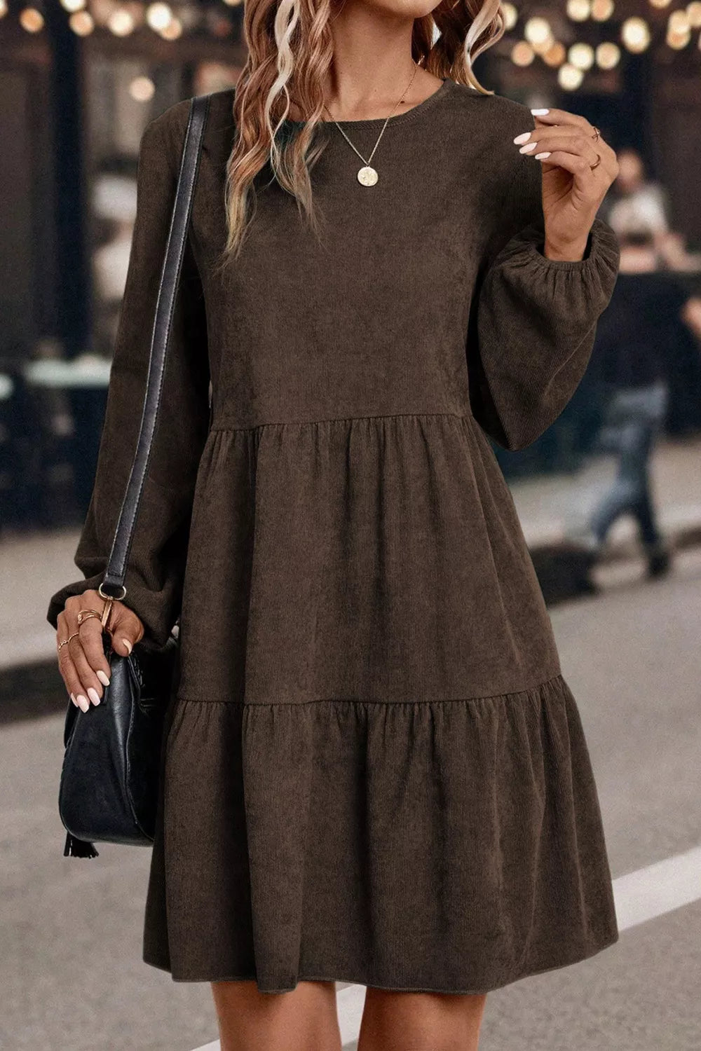Woman wearing a brown dress with long sleeves and a black handbag.