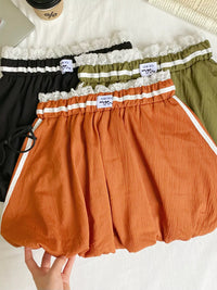 Three pairs of shorts in black, green, and orange with lace trim on a white surface.
