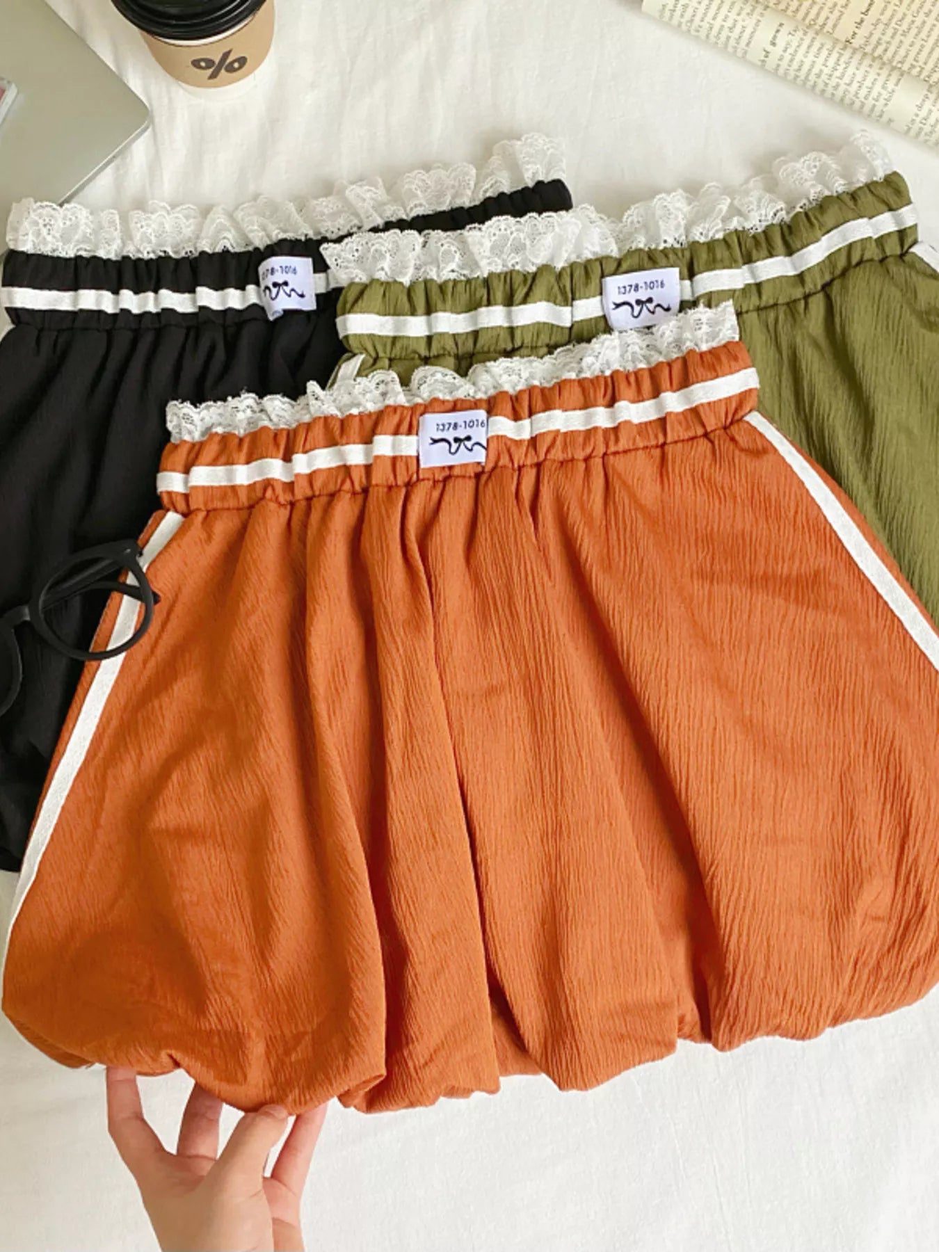 Three pairs of shorts in black, green, and orange with lace trim on a white surface.