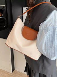 Person holding a beige and brown handbag with a visible brand logo.