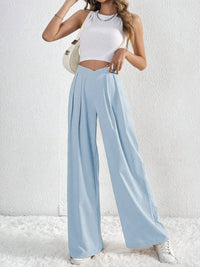 Woman wearing a white top and light blue wide-leg pants against a white background
