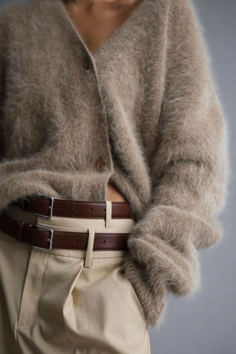 Person wearing a fluffy beige cardigan and beige pants with a belt, on a plain background