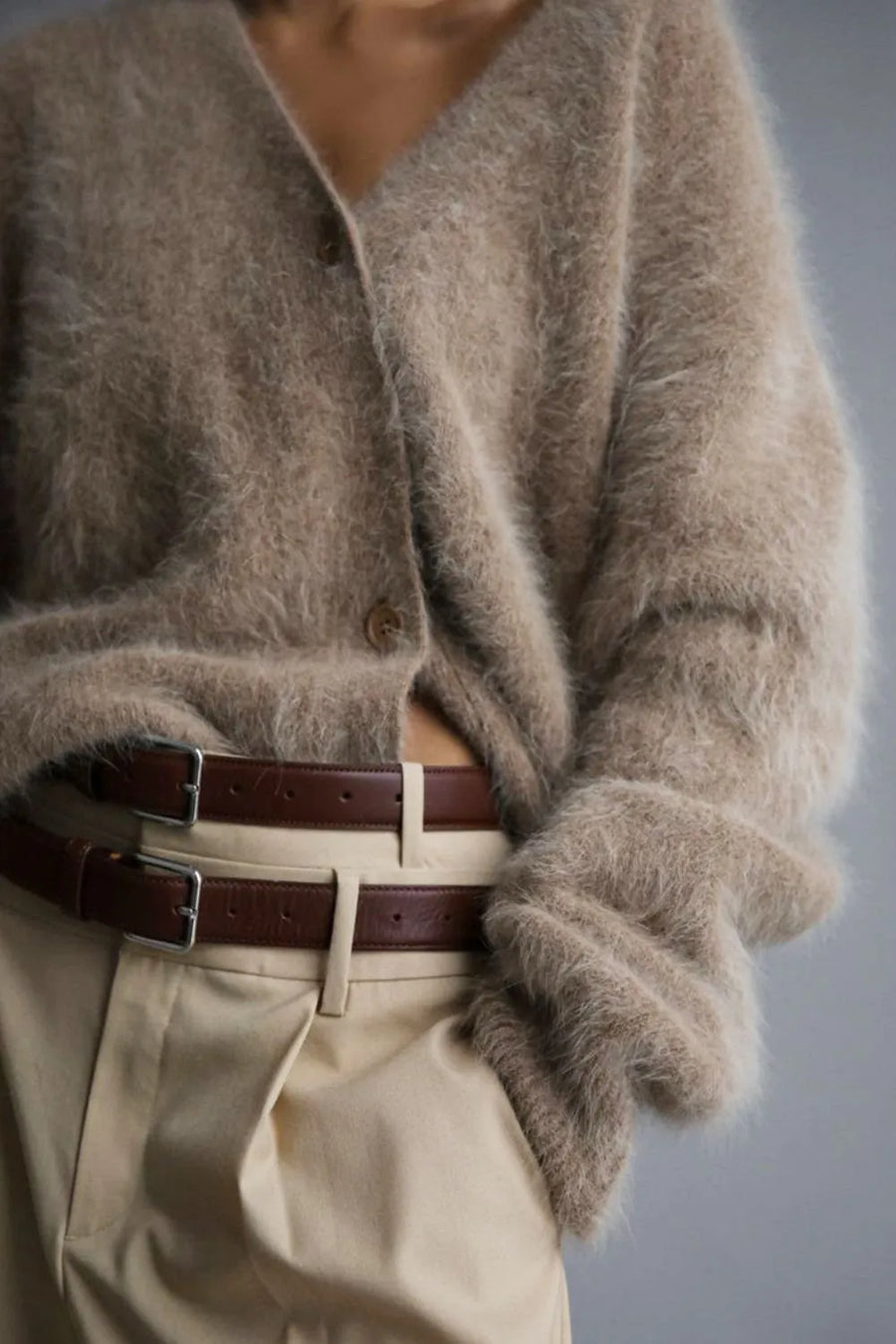 Person wearing a fluffy beige cardigan and beige pants with a belt, on a plain background