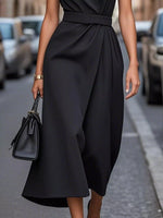 Person wearing a black dress holding a matching handbag on a street.