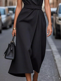 Person wearing a black dress holding a matching handbag on a street.