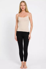Woman wearing a beige tank top and black leggings on a white background