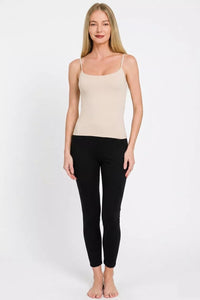 Woman wearing a beige tank top and black leggings on a white background