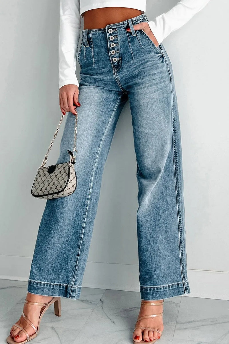 Person wearing high-waisted blue jeans with a white top and sandals, holding a small handbag.