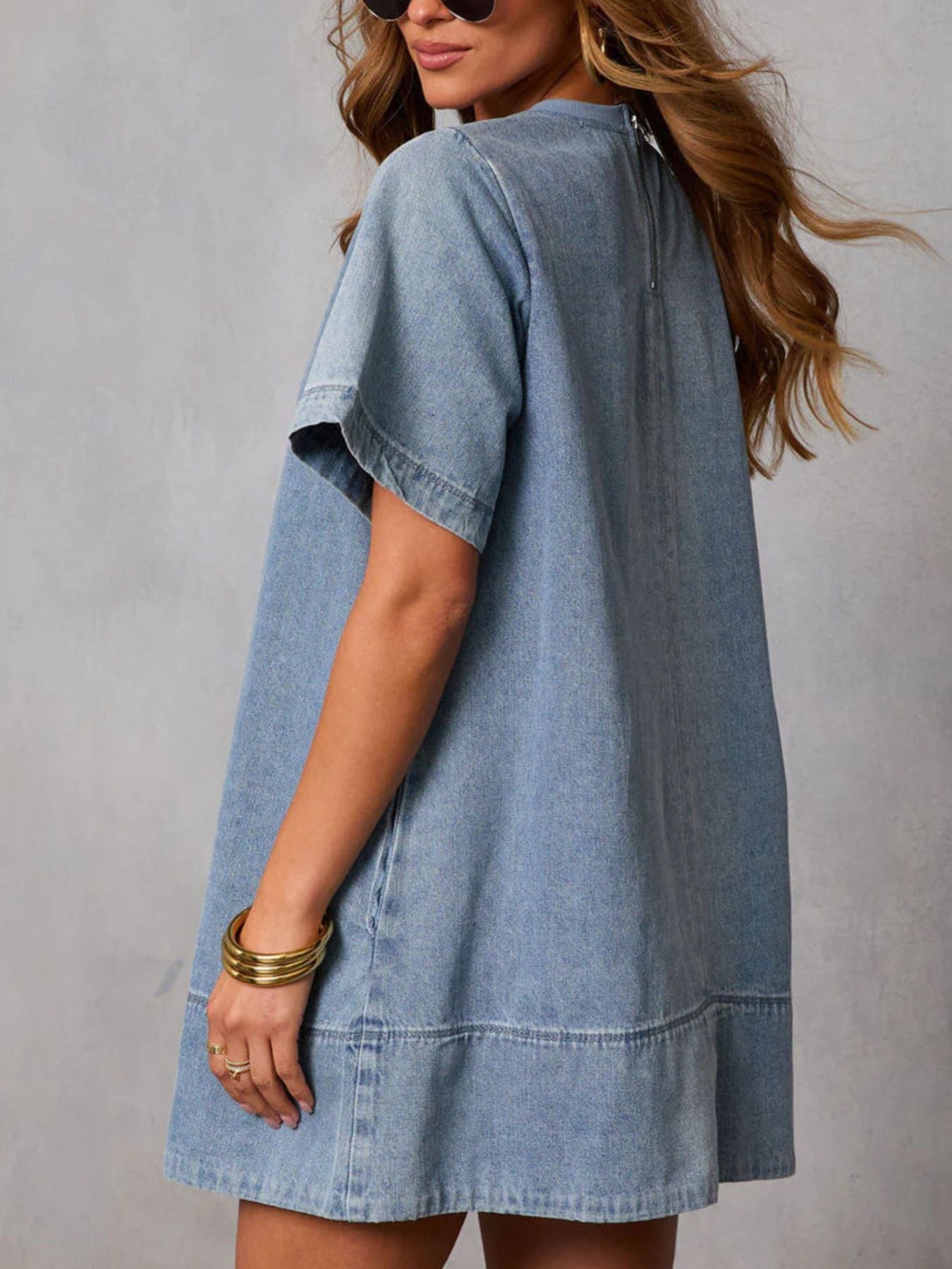 Woman wearing a light blue denim dress against a gray background