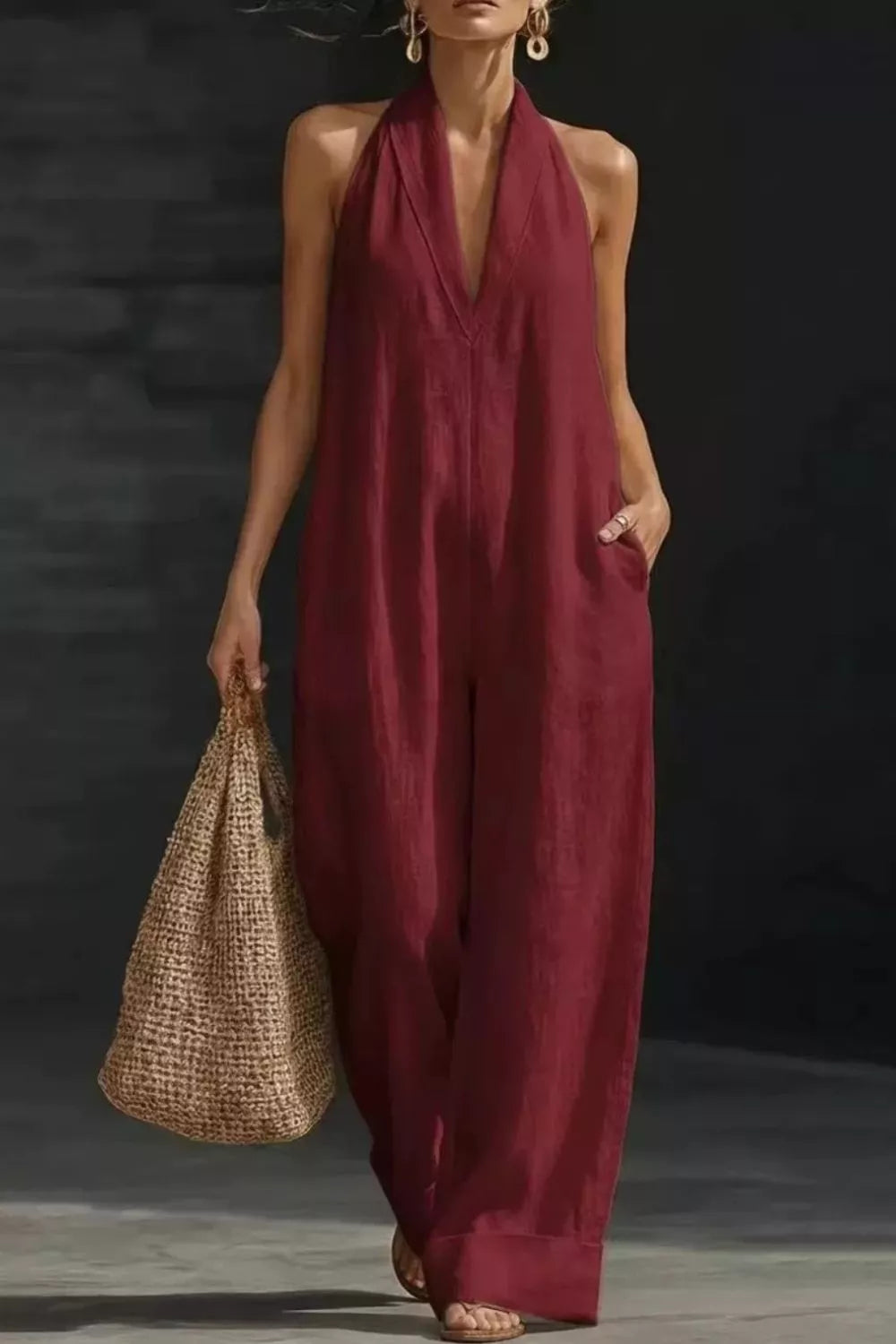 Woman wearing a burgundy jumpsuit holding a woven bag against a dark background