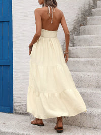 Woman in a long beige dress standing on stone steps with a blue door in the background